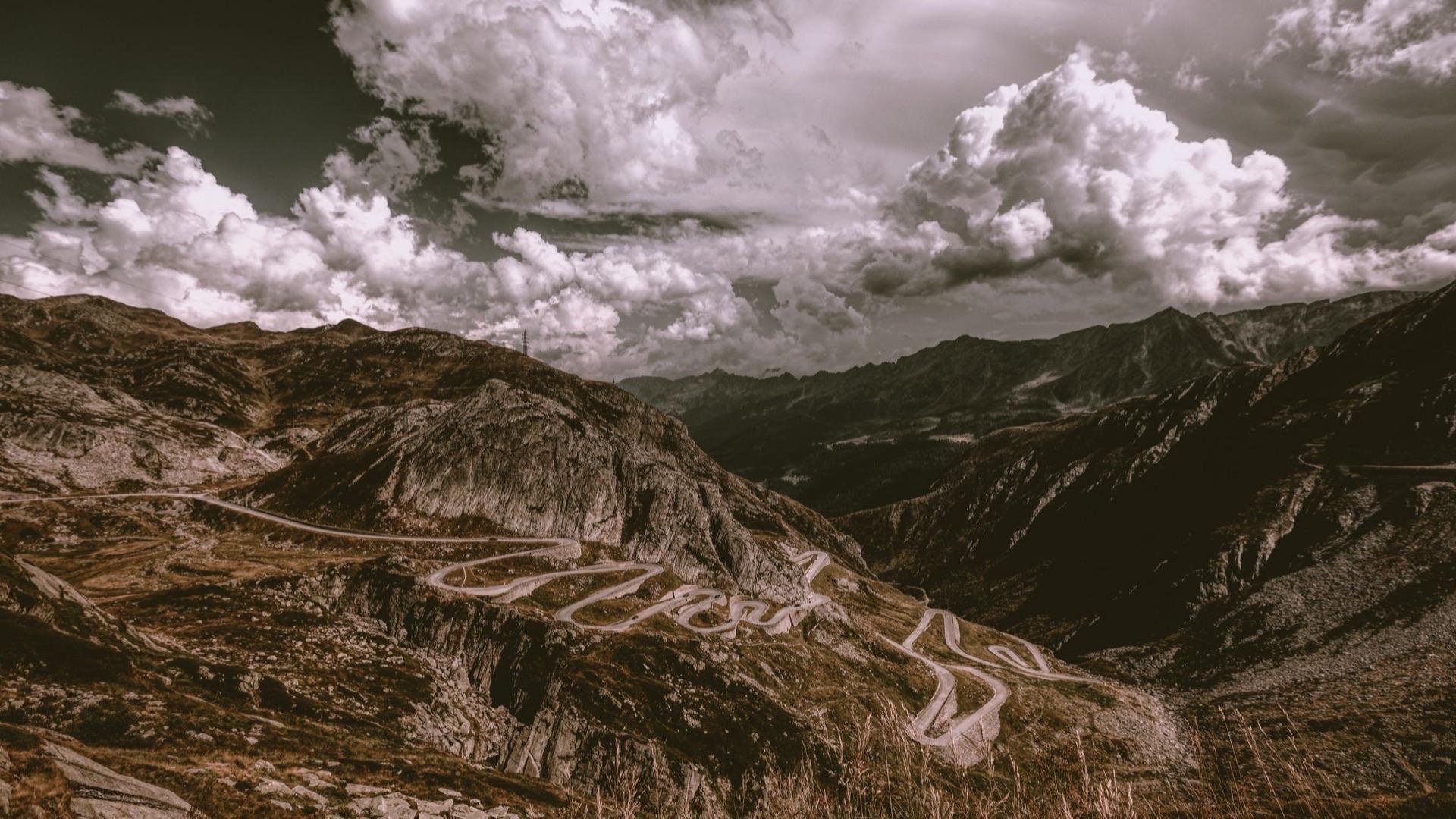 An old road switching back through a high mountain pass under heavy cloud.