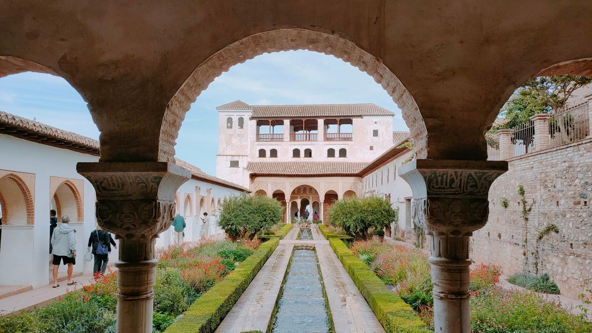 A carved stone arch framing a long courtyard pool between clipped hedges.